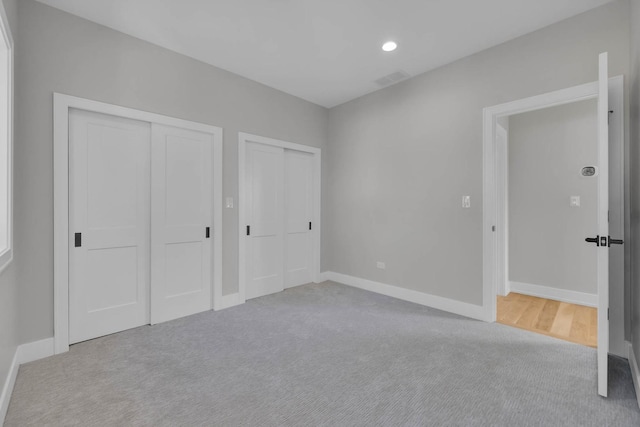 unfurnished bedroom featuring light carpet, baseboards, and multiple closets