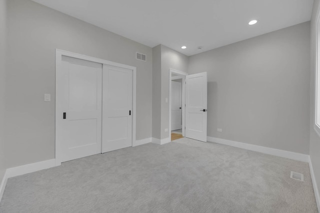 unfurnished bedroom with light carpet, a closet, visible vents, and baseboards