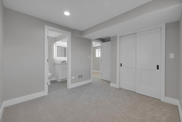 unfurnished bedroom featuring connected bathroom, light colored carpet, visible vents, baseboards, and a closet