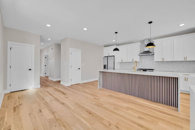 kitchen with a kitchen island with sink, light countertops, wall chimney range hood, stainless steel fridge, and pendant lighting