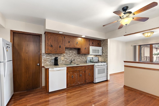 kitchen with white appliances, backsplash, sink, ceiling fan, and light hardwood / wood-style floors