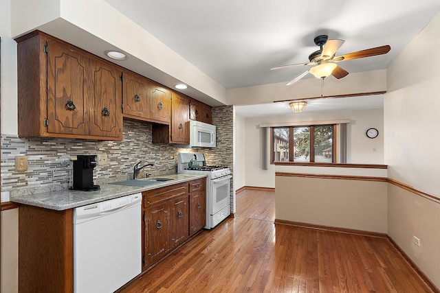 kitchen featuring white appliances, backsplash, sink, ceiling fan, and light wood-type flooring