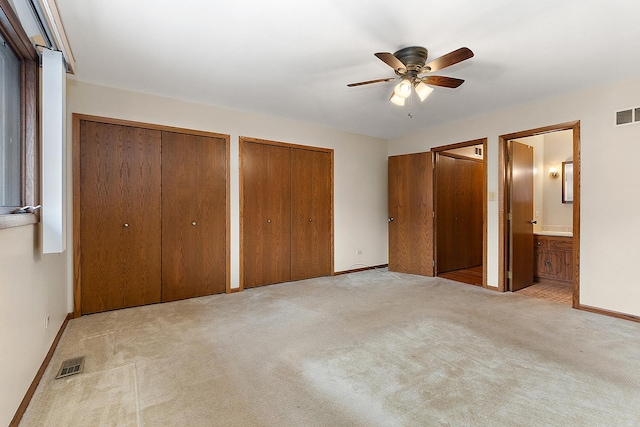 unfurnished bedroom featuring ceiling fan, two closets, light carpet, and ensuite bath