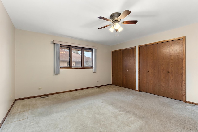 unfurnished bedroom with multiple closets, ceiling fan, and light colored carpet