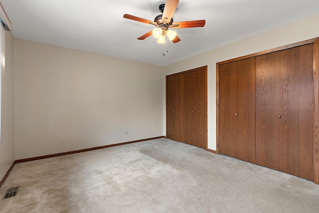 unfurnished bedroom featuring light carpet, ceiling fan, and multiple closets