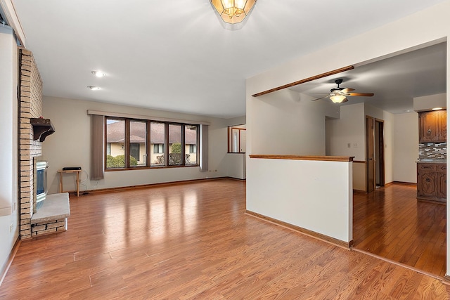 unfurnished living room with ceiling fan, a fireplace, and light hardwood / wood-style flooring