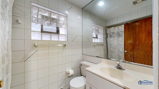 bathroom featuring vanity, toilet, tile walls, and walk in shower