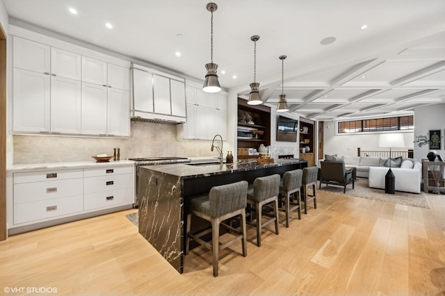 kitchen featuring a kitchen island with sink, light hardwood / wood-style flooring, coffered ceiling, and stainless steel range oven