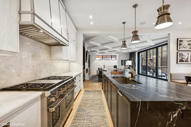 kitchen with pendant lighting, sink, coffered ceiling, wall chimney exhaust hood, and range with two ovens