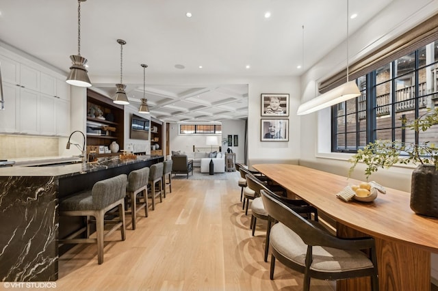 dining space with coffered ceiling, sink, and light hardwood / wood-style flooring