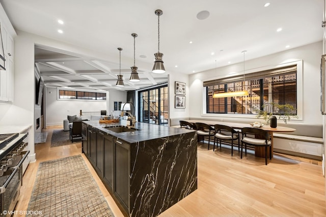 kitchen featuring sink, coffered ceiling, an island with sink, decorative light fixtures, and light wood-type flooring