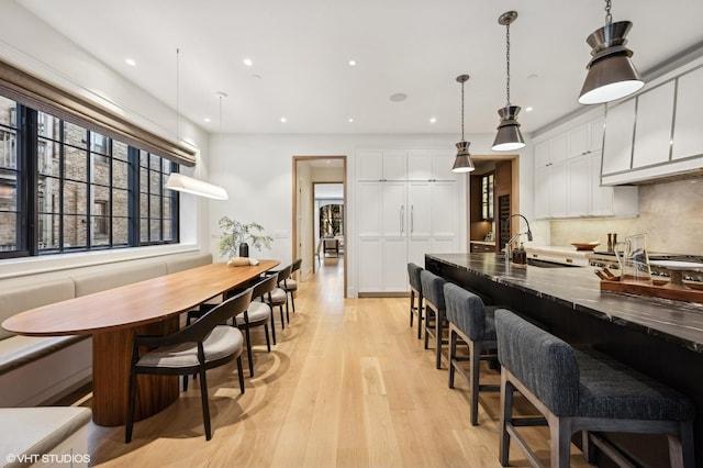 kitchen featuring pendant lighting, sink, light hardwood / wood-style floors, white cabinets, and decorative backsplash