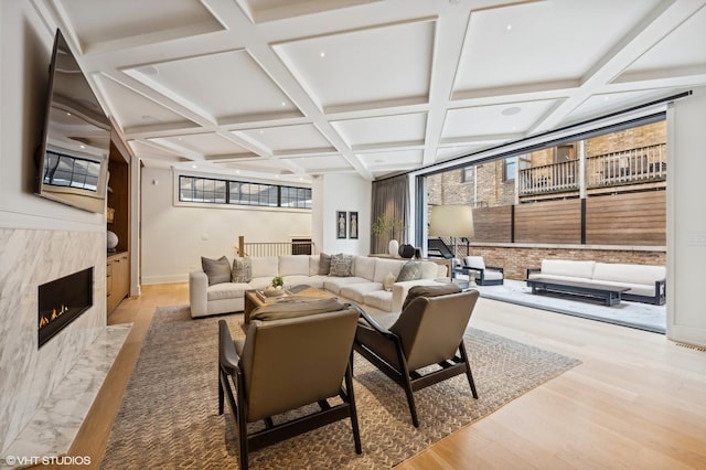 living room featuring a high end fireplace, coffered ceiling, light hardwood / wood-style floors, and beam ceiling