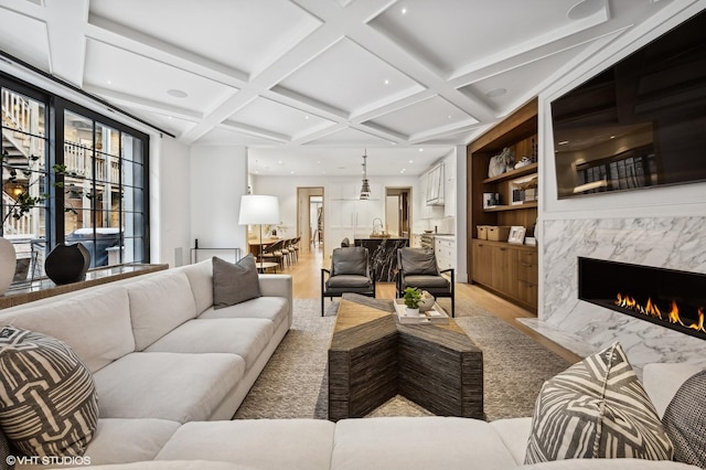 living room featuring a premium fireplace, coffered ceiling, built in features, and beam ceiling