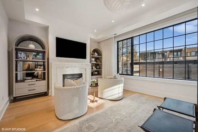 sitting room with built in shelves, a fireplace, and light wood-type flooring