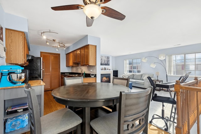 dining room with a tile fireplace, light hardwood / wood-style flooring, ceiling fan, and sink