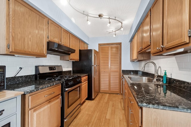 kitchen featuring backsplash, dark stone counters, stainless steel range with gas cooktop, sink, and light hardwood / wood-style floors