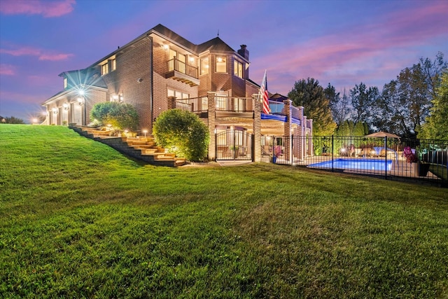 back house at dusk featuring a fenced in pool, a balcony, and a yard