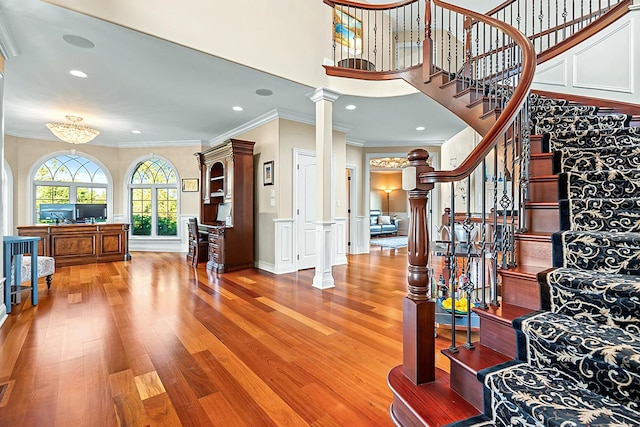 entrance foyer with a chandelier, hardwood / wood-style flooring, ornate columns, and crown molding