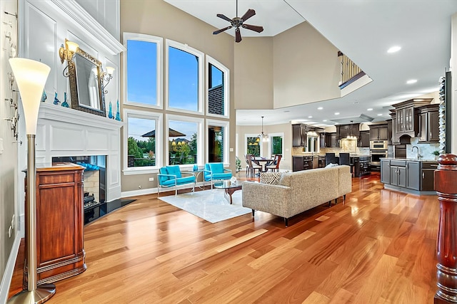 living room featuring a towering ceiling, light wood-type flooring, ceiling fan, and sink