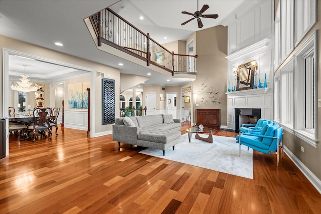 living room featuring ceiling fan with notable chandelier, wood-type flooring, and a high ceiling