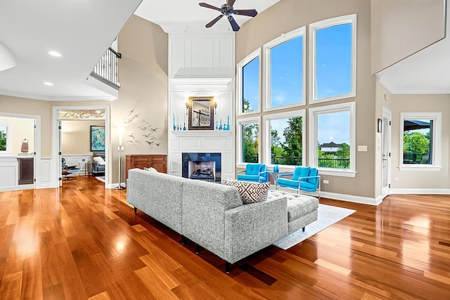 living room with ceiling fan, a large fireplace, a towering ceiling, and hardwood / wood-style flooring