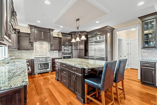 kitchen featuring high end appliances, sink, hanging light fixtures, decorative backsplash, and a kitchen island