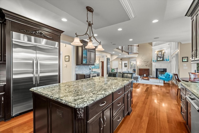 kitchen featuring dark brown cabinetry, decorative light fixtures, stainless steel built in fridge, a fireplace, and a kitchen island