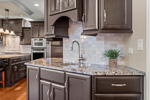 kitchen with dark brown cabinetry, stainless steel double oven, tasteful backsplash, light hardwood / wood-style flooring, and decorative light fixtures