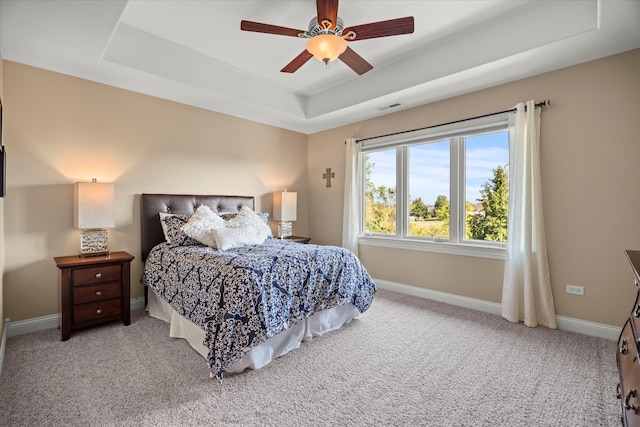 carpeted bedroom with a raised ceiling and ceiling fan