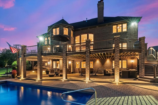 back house at dusk featuring a balcony, an outdoor hangout area, and a patio