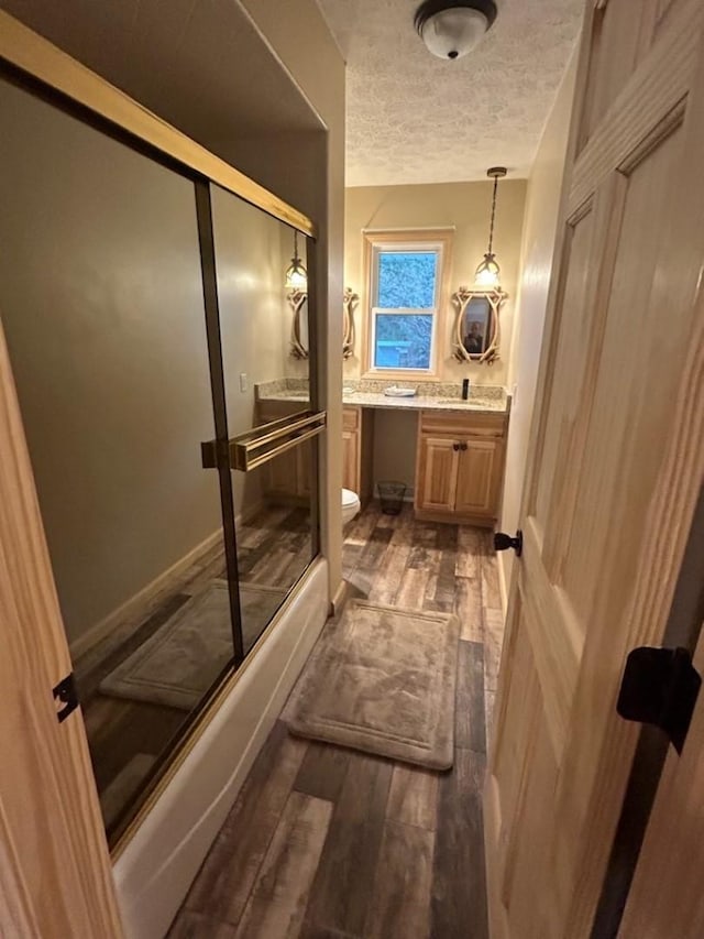 full bathroom featuring bath / shower combo with glass door, vanity, a textured ceiling, hardwood / wood-style floors, and toilet