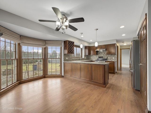 kitchen featuring decorative backsplash, appliances with stainless steel finishes, light hardwood / wood-style flooring, and pendant lighting