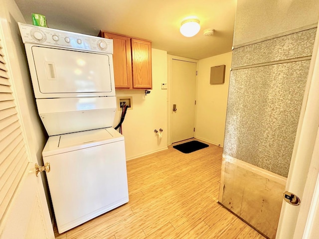 laundry room with light wood-style floors, cabinet space, and stacked washing maching and dryer