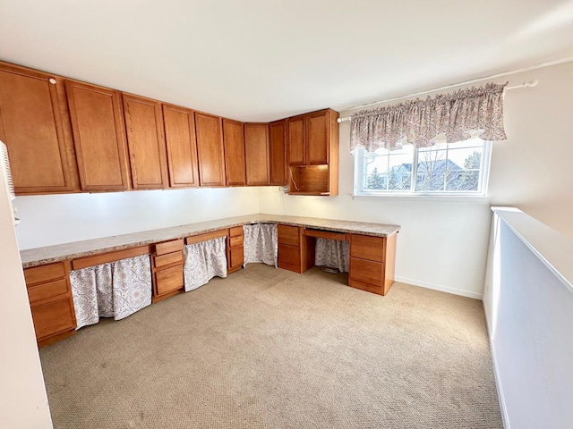 unfurnished office with baseboards, built in desk, and light colored carpet