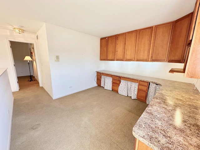 unfurnished office featuring light colored carpet, built in desk, and baseboards