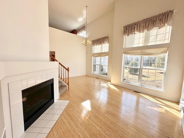 unfurnished living room featuring visible vents, a towering ceiling, light wood-style flooring, stairway, and a fireplace