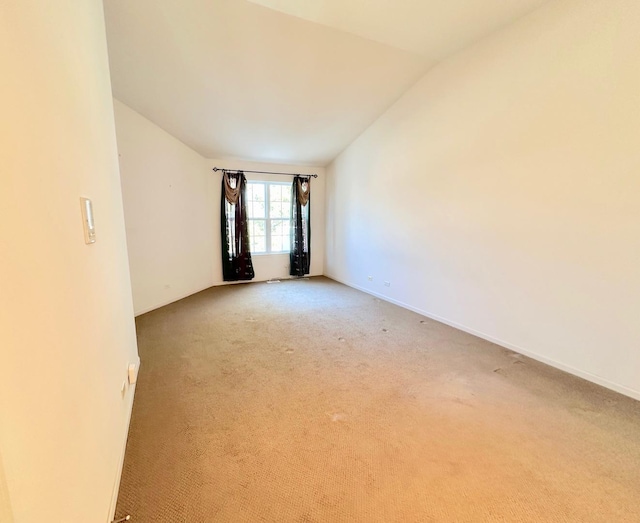 empty room featuring light colored carpet, vaulted ceiling, and baseboards