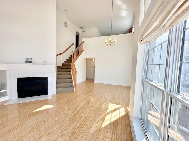 unfurnished living room featuring a fireplace, stairway, a high ceiling, wood finished floors, and a chandelier