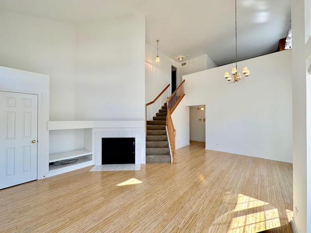 unfurnished living room featuring a tile fireplace, wood finished floors, a towering ceiling, stairs, and an inviting chandelier