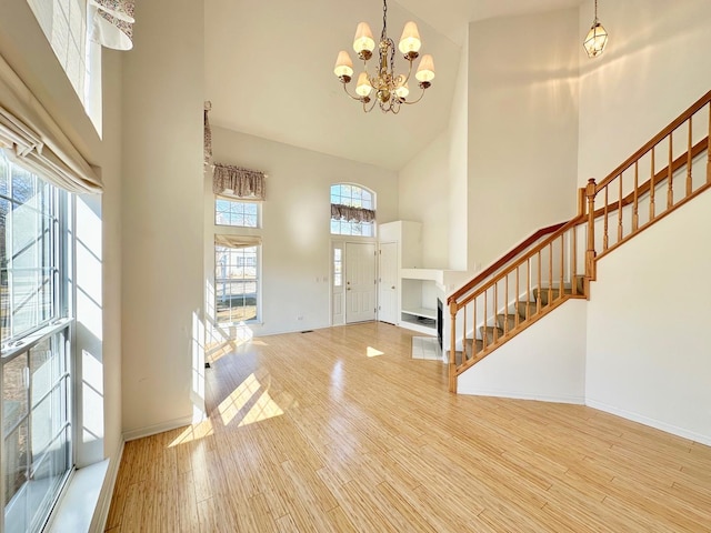 entryway featuring stairway, a towering ceiling, wood finished floors, a chandelier, and baseboards