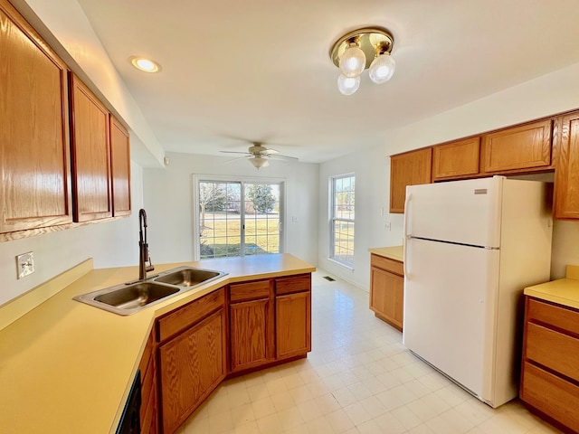 kitchen with brown cabinets, freestanding refrigerator, a peninsula, light countertops, and a sink