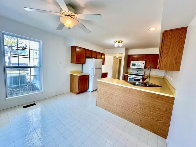 kitchen featuring a peninsula, white appliances, a sink, visible vents, and light countertops