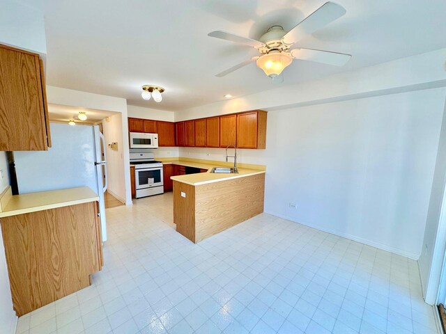 kitchen featuring a peninsula, white appliances, a sink, light countertops, and light floors