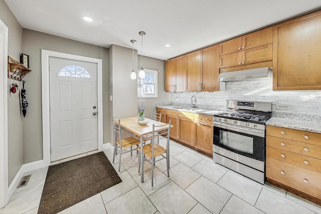 kitchen with sink, hanging light fixtures, stainless steel gas range, light stone counters, and decorative backsplash