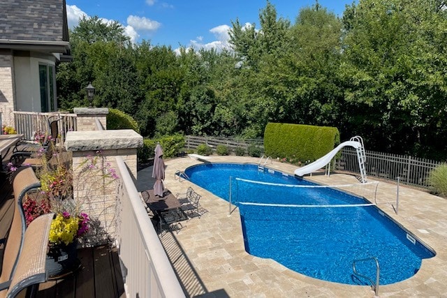 view of swimming pool with a water slide, a diving board, and a patio