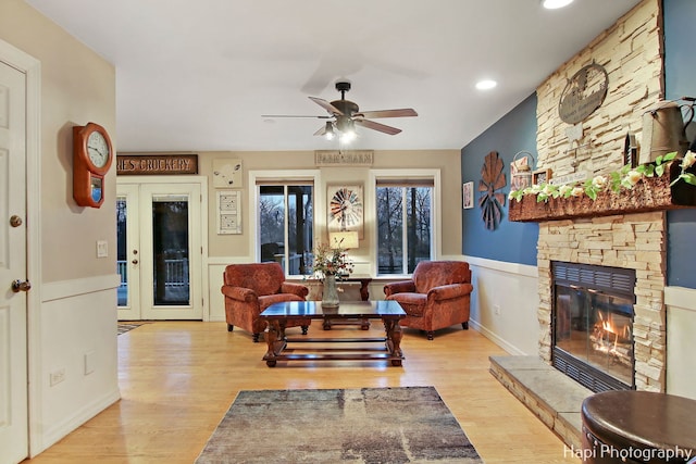 living room featuring a stone fireplace, ceiling fan, french doors, and light hardwood / wood-style floors