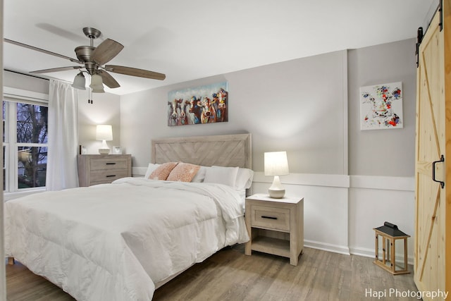 bedroom with hardwood / wood-style flooring, ceiling fan, and a barn door