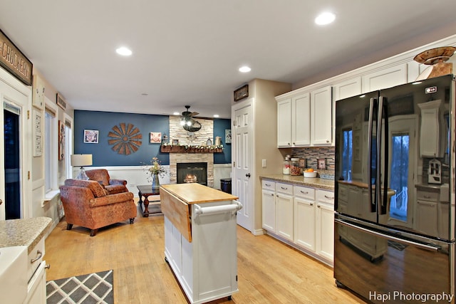 kitchen with black refrigerator, white cabinets, a stone fireplace, and light hardwood / wood-style flooring