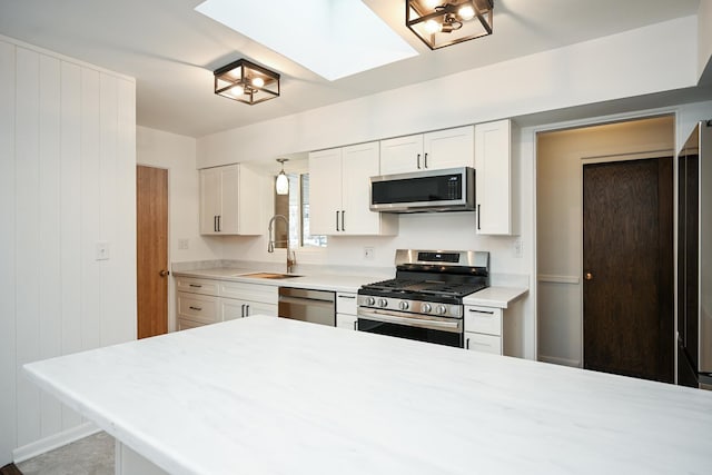 kitchen featuring sink, wooden walls, a skylight, white cabinetry, and stainless steel appliances